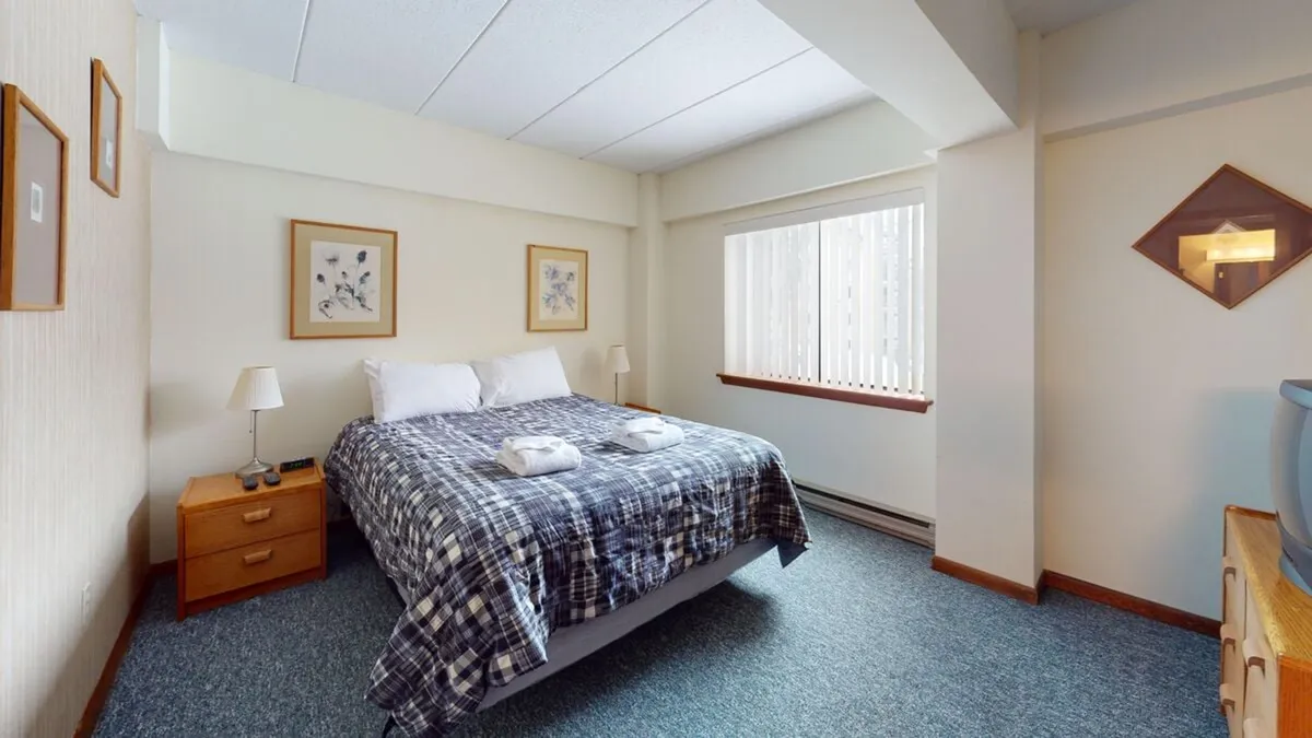 Here, a bedroom is shown with a comfortable bed, a window allowing natural light, framed artwork, a nightstand, and a lamp. The inviting mood is enhanced by the sunlight streaming in, highlighting the room as a peaceful retreat.
