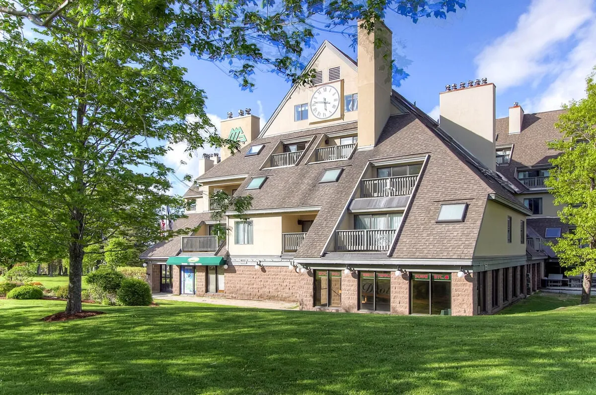 A view of the resort’s exterior featuring a large clock, green awning, multiple balconies, and a lush green lawn. This outdoor space radiates a welcoming vibe, hinting at relaxed socializing, outdoor events, and the potential for gatherings.