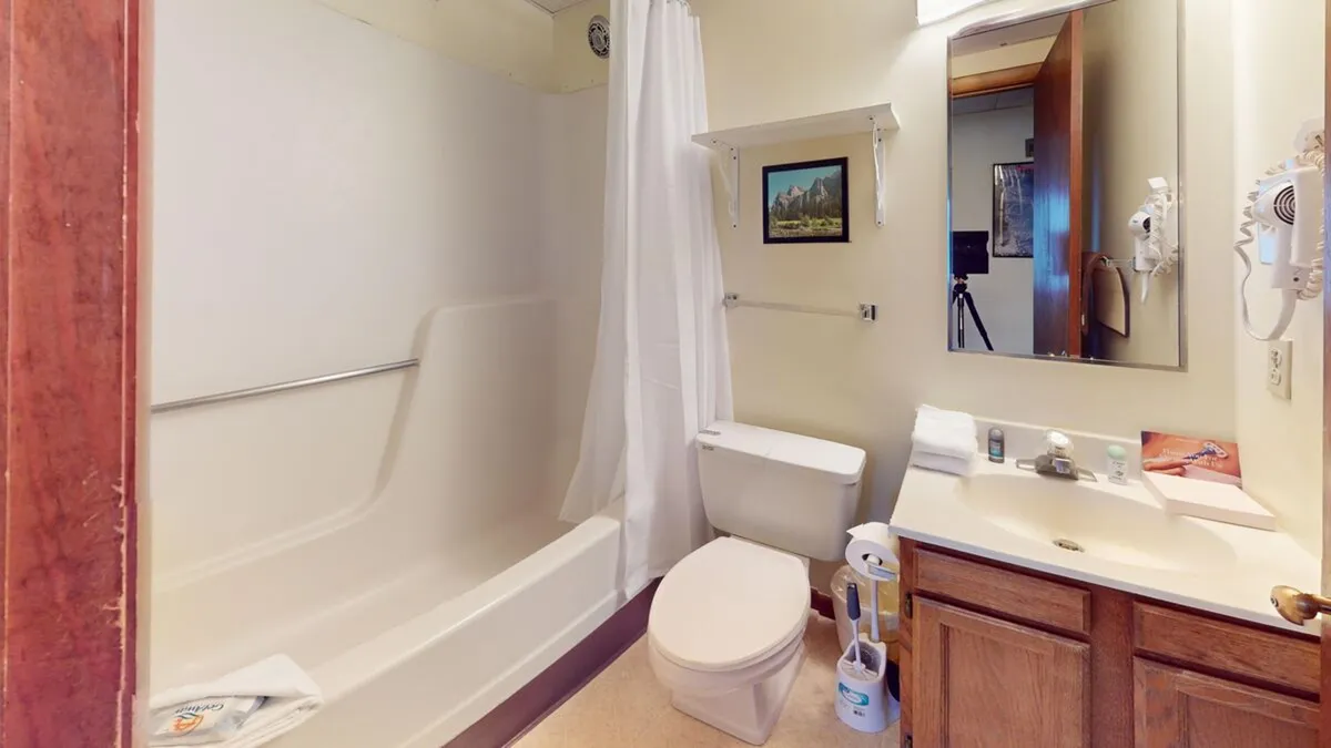 This bathroom image features a bathtub, toilet, sink, mirror, and wall art. The setup is simple, practical, and exudes a peaceful vibe—perfect for unwinding or refreshing after a day of adventure.