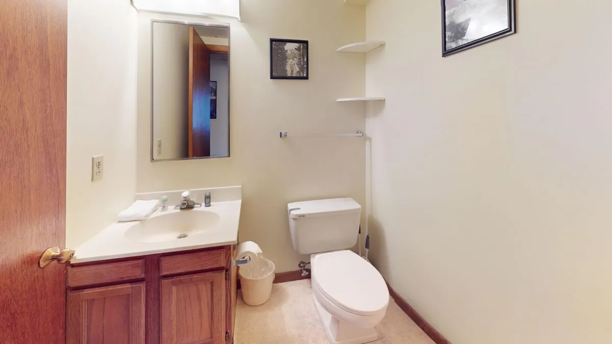 A compact yet functional bathroom with a mirror, sink, toilet, and framed picture above. The mood is practical and serene, offering a spot for quick refreshment and personal care.