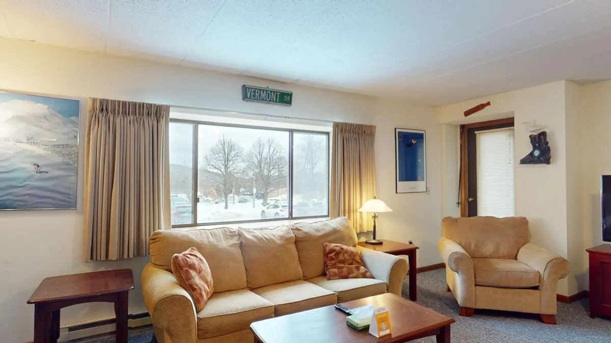 The image shows a cozy living area featuring a comfortable sofa positioned by a large window that lets in abundant natural light. A stylish lamp and a coffee table sit nearby, inviting guests to relax, read, or enjoy a board game. The ambiance is warm and welcoming, perfect for unwinding after a day on the slopes or the golf course.