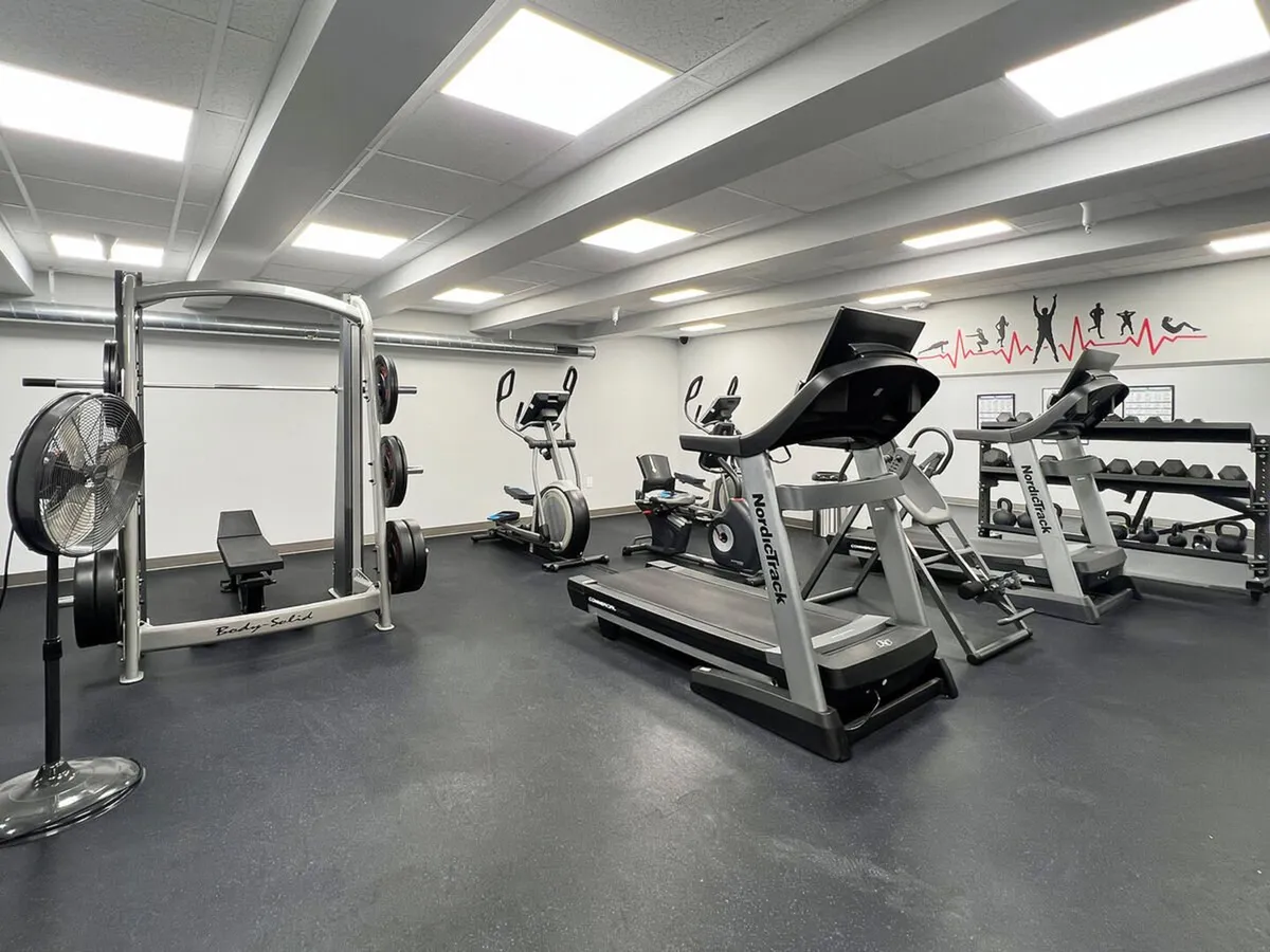 This energetic interior shot focuses on a well-equipped fitness center, including a weightlifting machine, treadmill, exercise bike, and dumbbell rack. The space is bright and motivational, inviting guests to pursue personal fitness goals year-round.