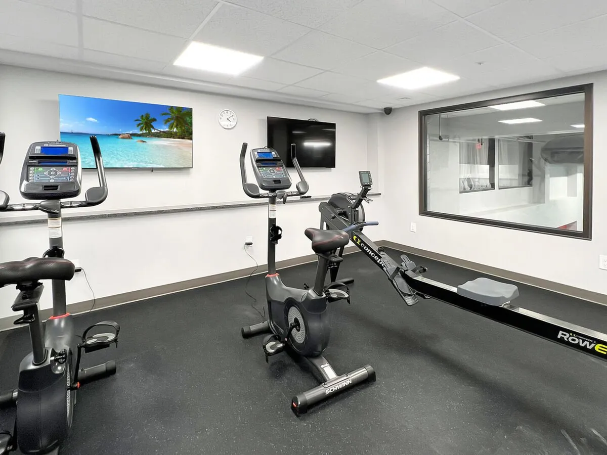 A modern fitness room equipped with exercise bikes, a rowing machine, a TV showing a calming beach scene, and plenty of light. The space feels energetic yet welcoming, inviting guests to maintain their routines during their stay.