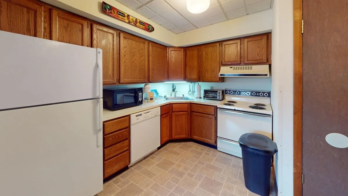 This image reveals a practical kitchen space with wood cabinetry, white appliances, and a spacious counter area. The microwave and visible accessories suggest readiness for both day-to-day cooking and special family gatherings. The overall setup exudes an inviting, functional environment ideal for preparing meals together.