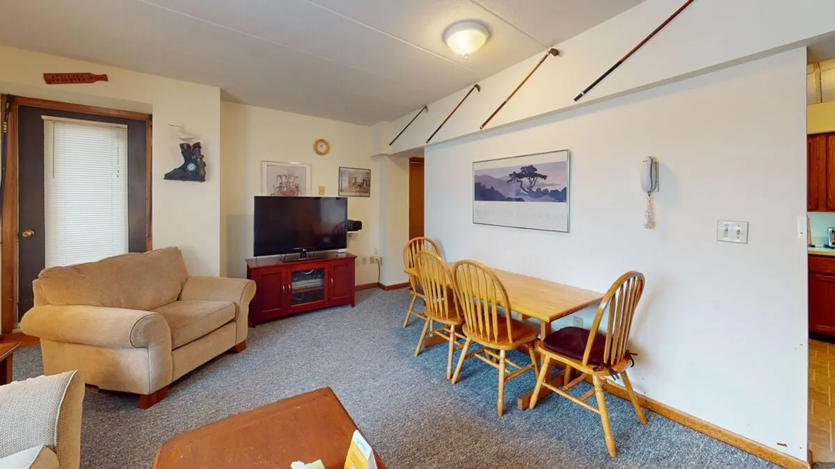 A spacious open-plan living and dining area. The image includes a cozy sofa, a well-sized dining table for gatherings or games, a television for entertainment, and tasteful wall art. The arrangement is conducive to family activities, meals, and movie nights in a warm, communal setting.