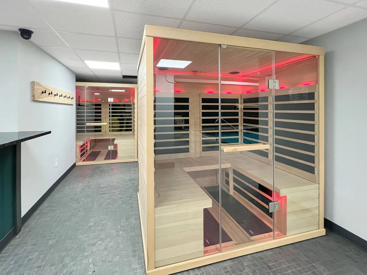 A tranquil, glass-walled infrared sauna with ambient lighting, offering a serene retreat for guests seeking relaxation and rejuvenation. The clean, modern design creates a sense of calm and wellness.