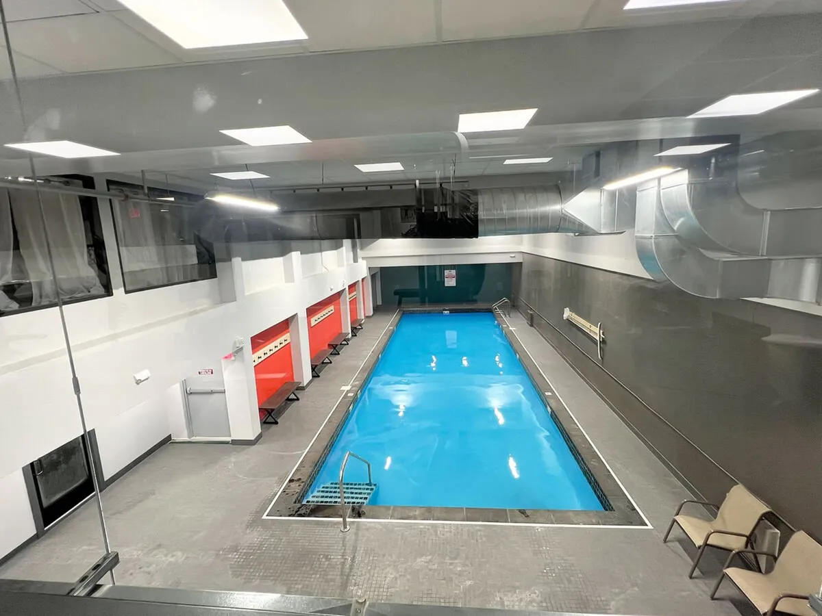 A spacious indoor swimming pool with clear blue water, surrounded by lounge chairs and adjacent changing rooms. The bright, airy environment invites guests to swim, relax, or socialize regardless of the season.