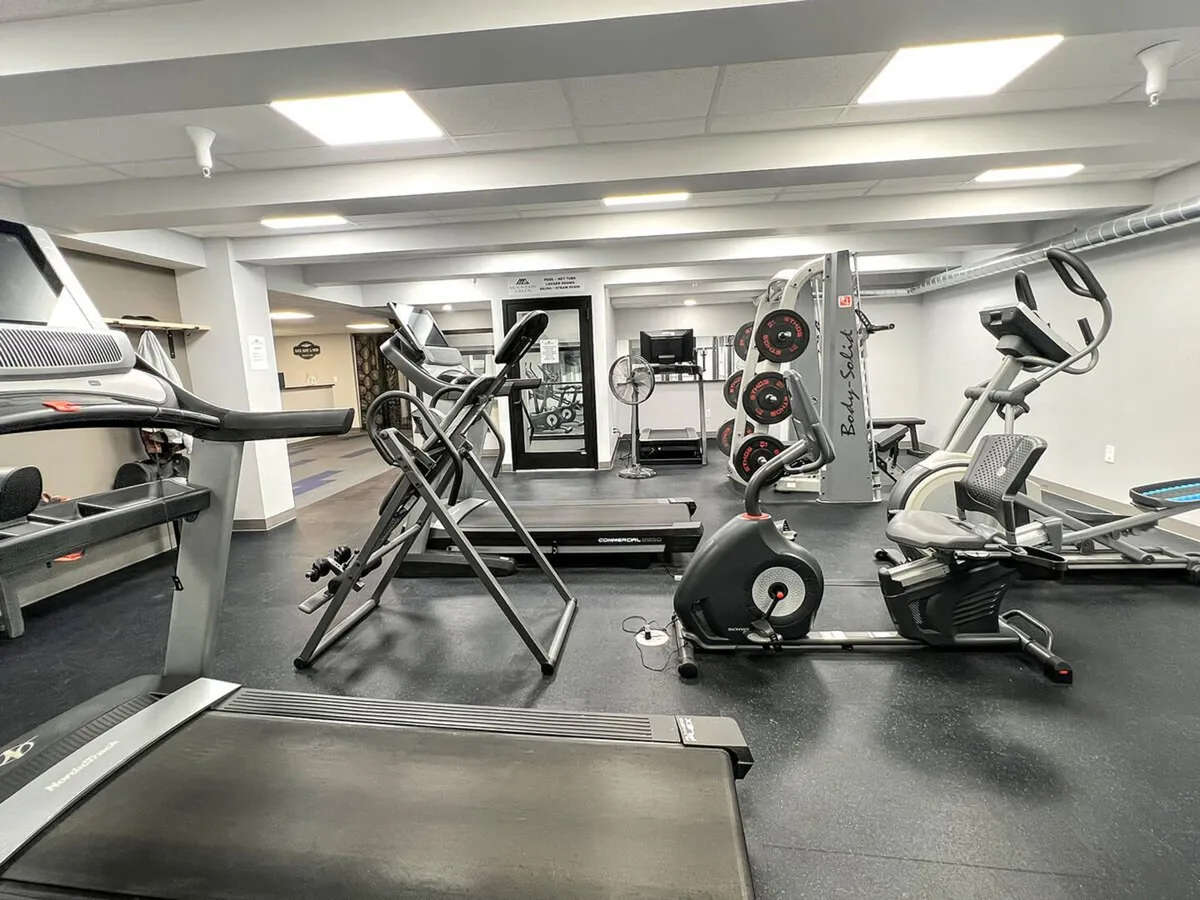 A well-equipped fitness center showcasing a variety of workout equipment including treadmills, elliptical machines, a weight rack, and an exercise bike. The space feels modern and energetic, encouraging guests to focus on their fitness goals.