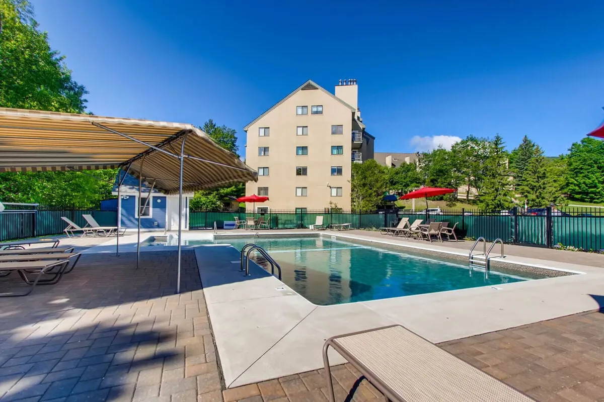 This exterior image features a vibrant outdoor swimming pool surrounded by lounge chairs, red umbrellas, and lush greenery. The inviting pool area is clearly designed for relaxation, sunbathing, and socializing, with space for group activities like poolside barbecues.
